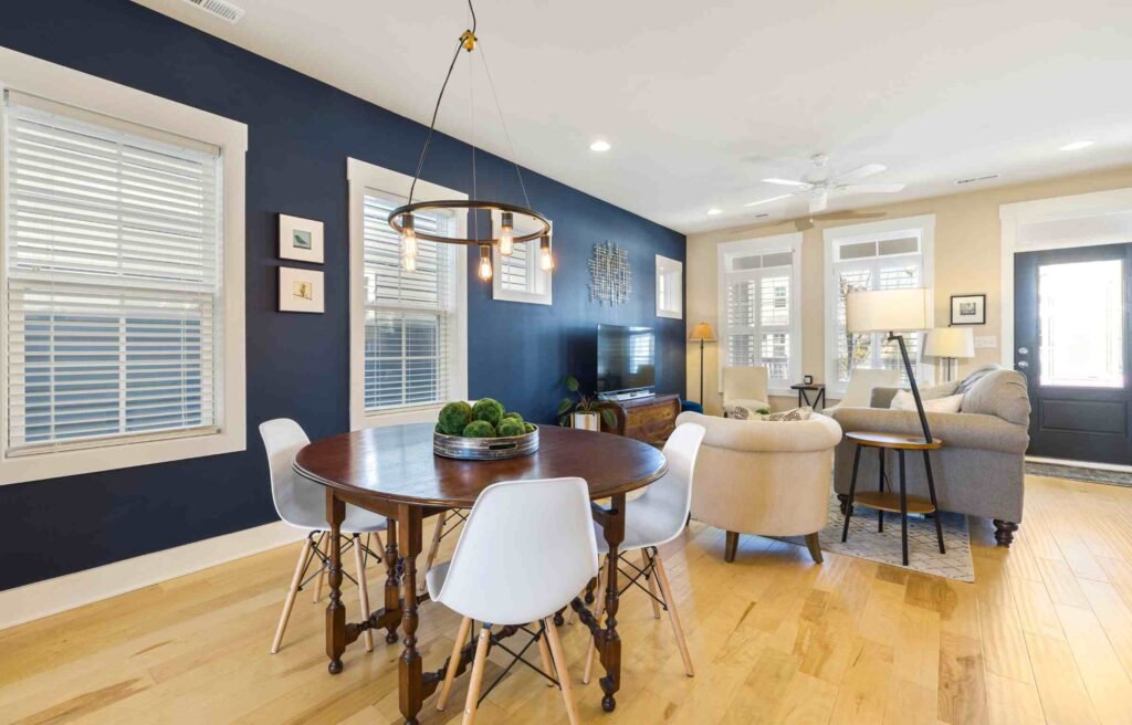 Modern living room with wooden floor, navy wall, round table, and white chairs.